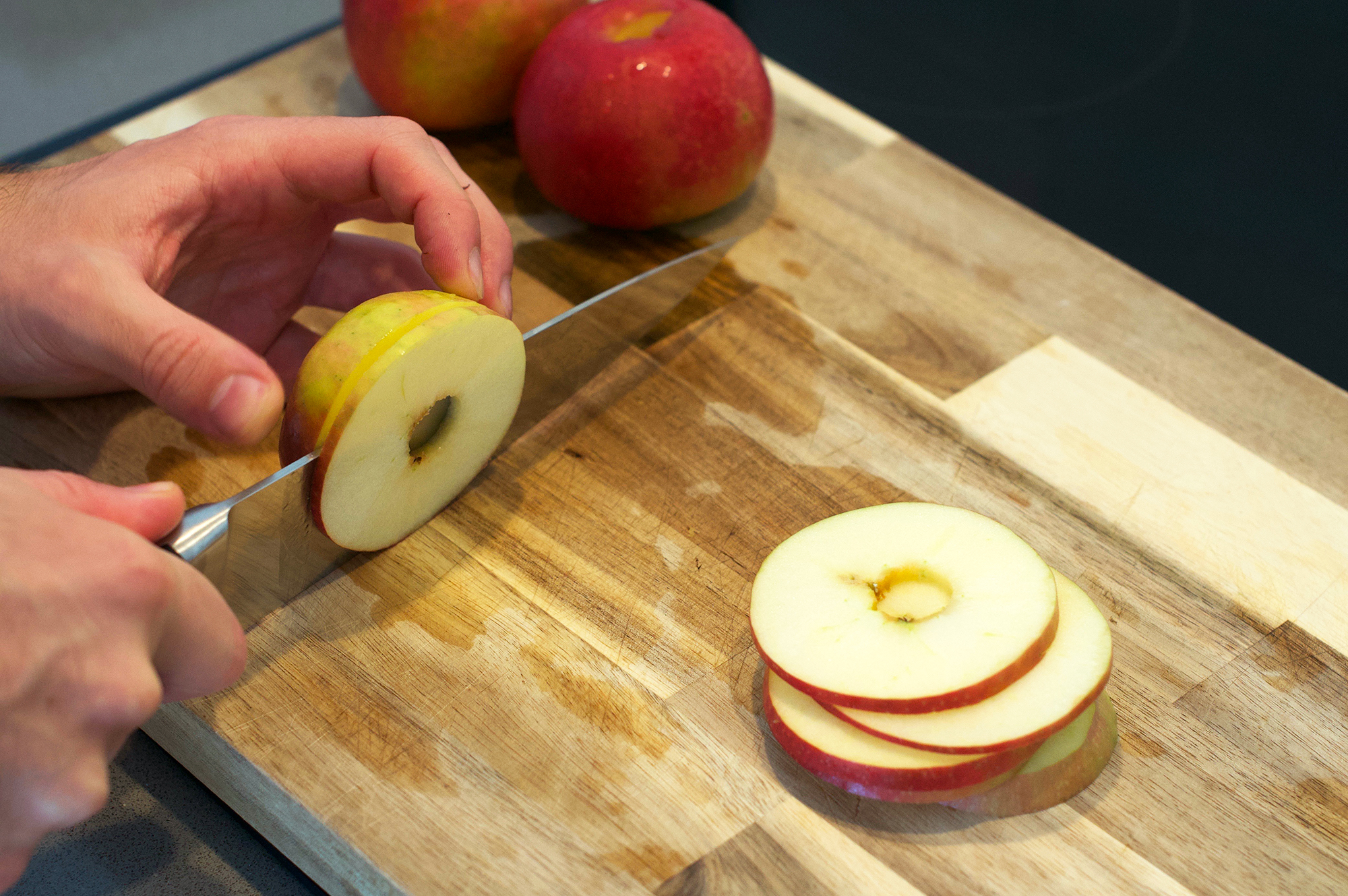 Slicing cored apples on wooden chopping board